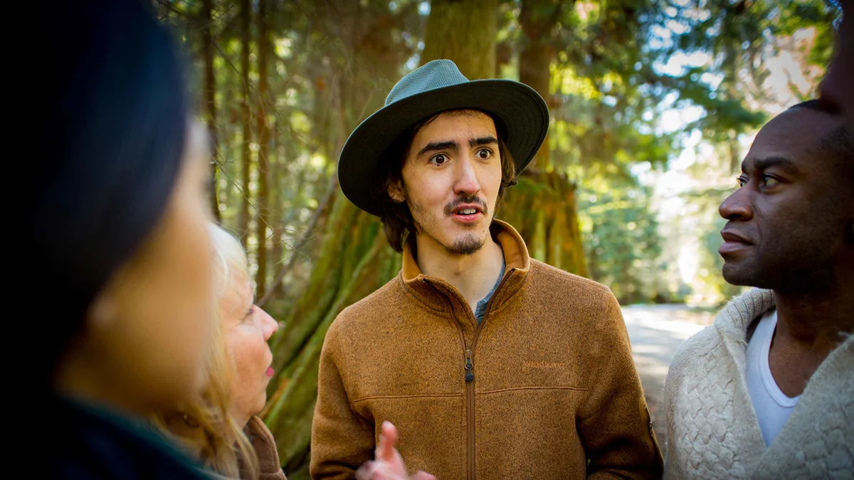 Walking tour group among old-growth stumps on a hidden Stanley Park trail, dark secrets of Stanley Park tour Vancouver