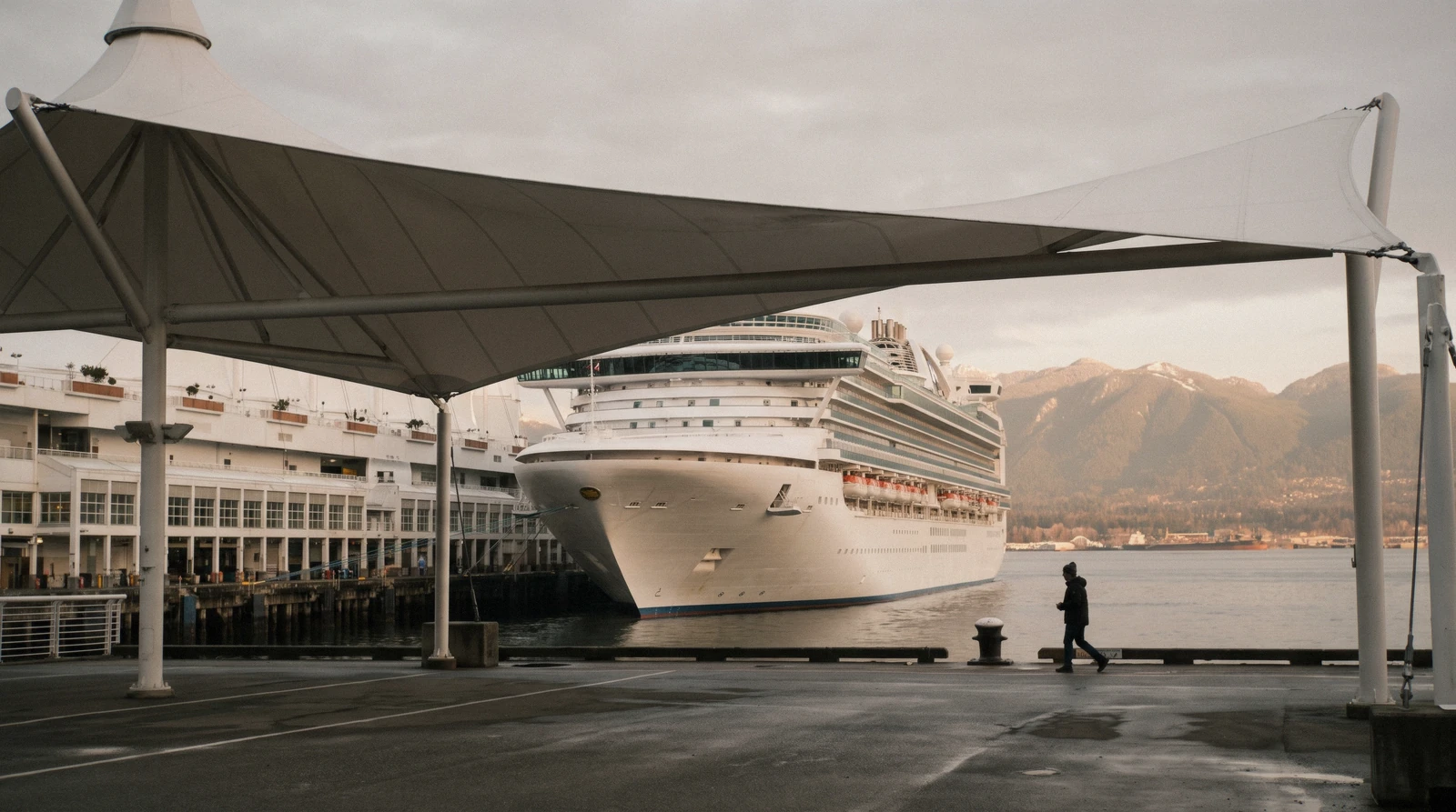 A cruise ship berthed beneath the five white sails of the terminal with the North Shore mountains behind, the Vancouver cruise port on an Alaska sailing day